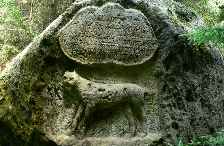 Foto eines Felsens, in den ein Luchs und eine Inschrift gehauen wurden.
