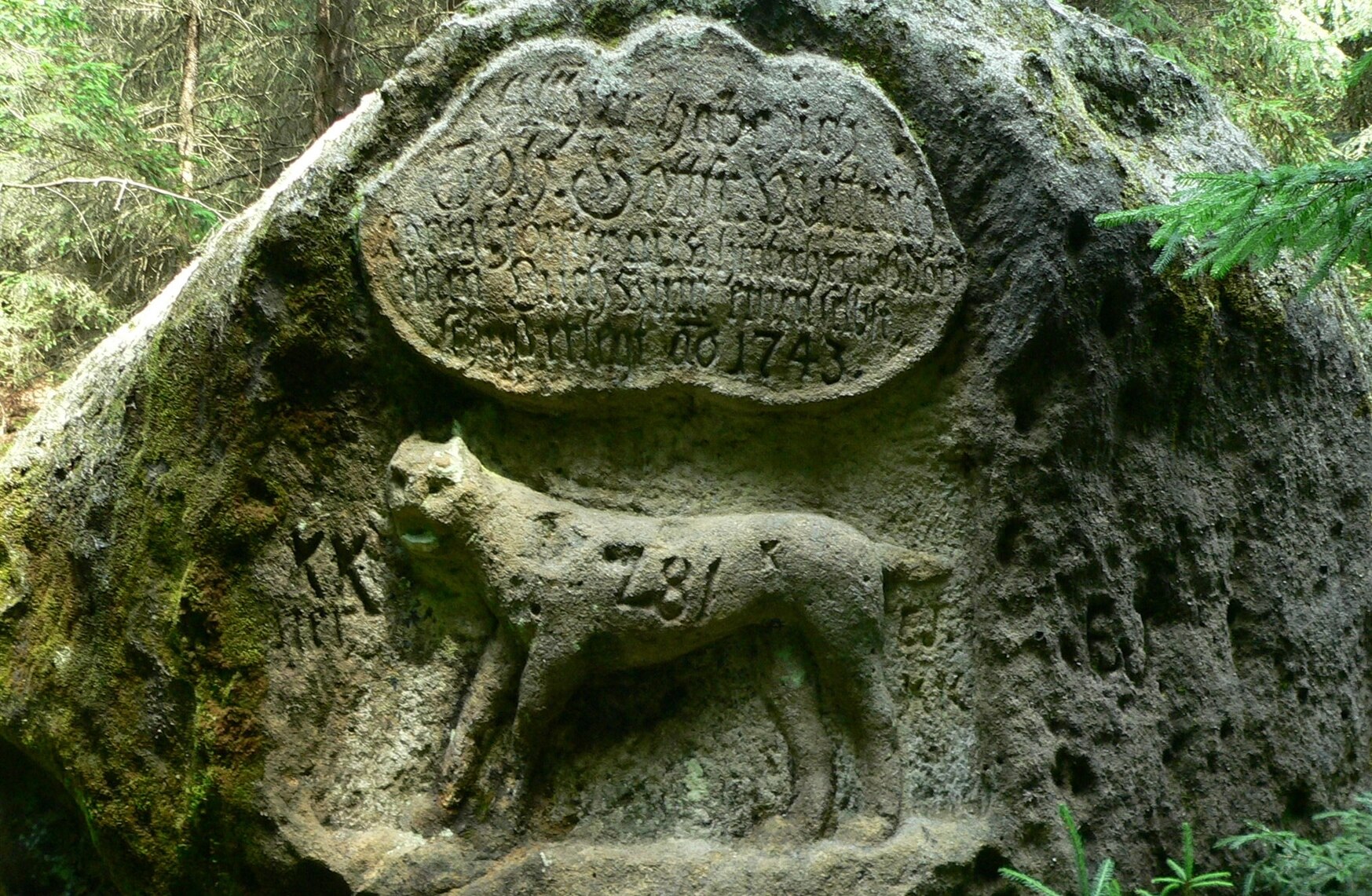 Foto eines Felsens, in den ein Luchs und eine Inschrift gehauen wurden.